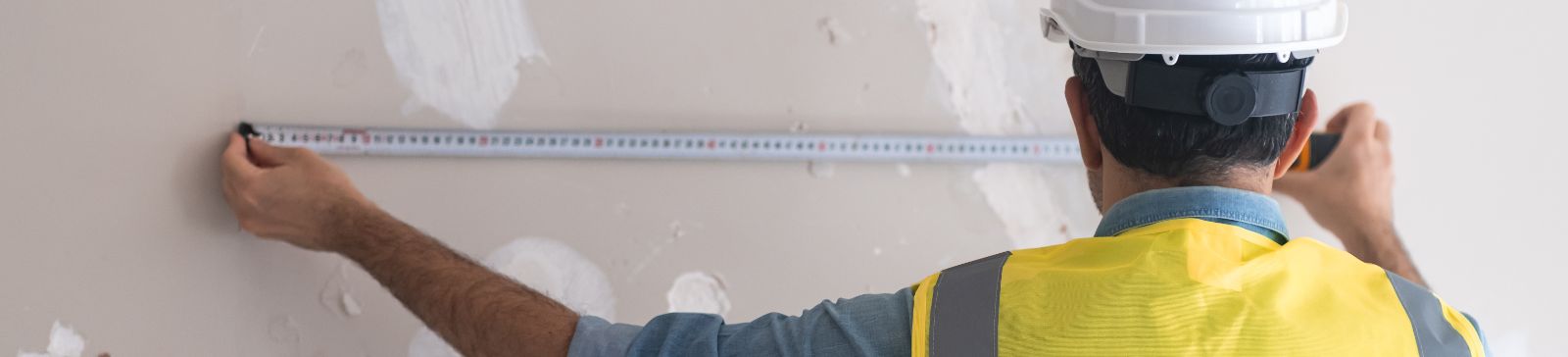 A male worker measuring wall while remodeling