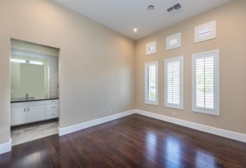 Remodeled living room in Whittier with dark hardwood floors, tall windows with white shutters, and a modern bathroom vanity in view.