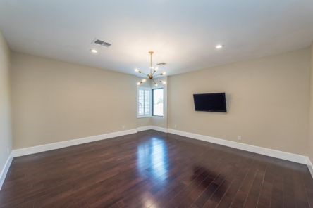 Modern living room in Whittier with dark hardwood floors, corner windows with shutters, and a stylish chandelier for a contemporary touch.