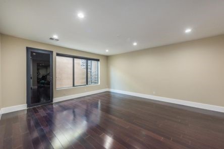 Modern living room in Whittier with dark hardwood floors, corner windows with shutters, and a stylish chandelier for a contemporary touch.