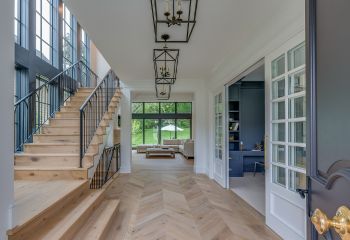 Bright South Whittier entryway with herringbone hardwood floor, black double doors, and modern geometric light fixtures.