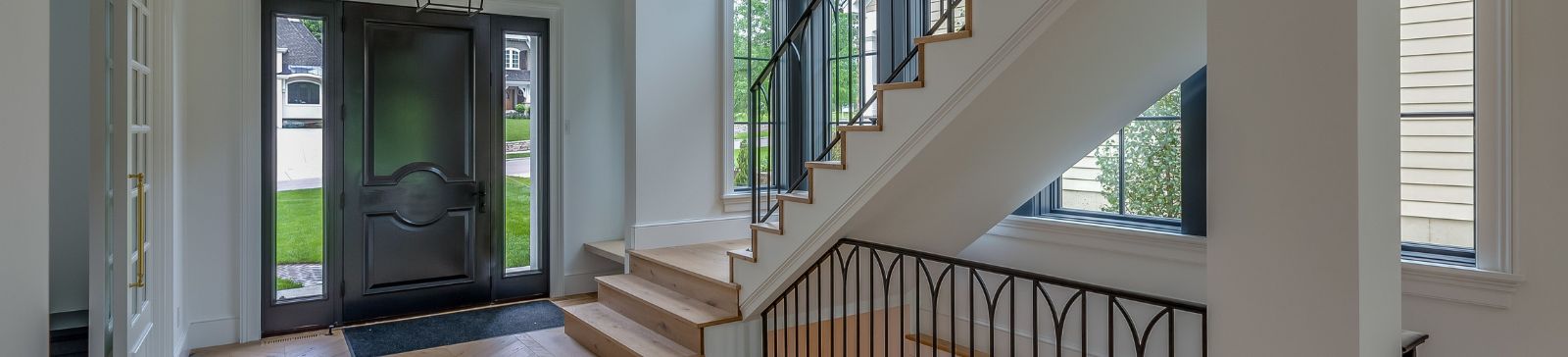 Open-concept living room and stairway in South Whittier luxury home featuring natural wood floors, glass doors, and elegant black railings.